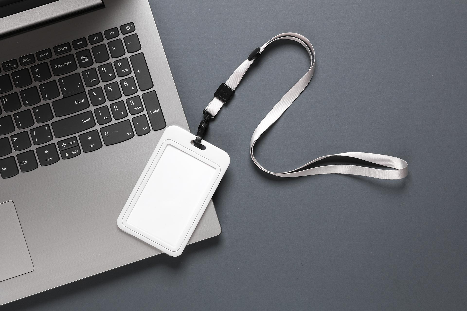 An ID badge with a lanyard placed next to a laptop keyboard on a dark surface